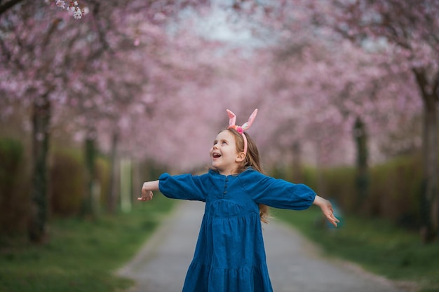 Páscoa Menina bonita com cabelo longo encaracolado com orelhas de coelho em flores de cerejeira Férias de primavera