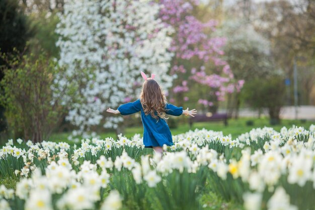 Páscoa Menina bonita de 5 anos com orelhas de coelho no gramado de narcisos Criança feliz Férias de primavera