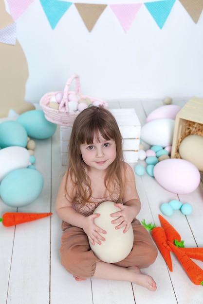 Páscoa! Menina bonita em um branco com ovos de Páscoa coloridos, cesta de Páscoa e lebres. Decoração de Páscoa, decorações de primavera em casa. Férias em família, tradições. colheita, pequeno agricultor.