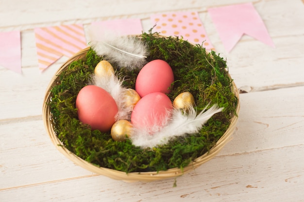 Páscoa. Os ovos da páscoa coloridos encontram-se em uma cesta em um fundo branco de madeira. Feriado de primavera.