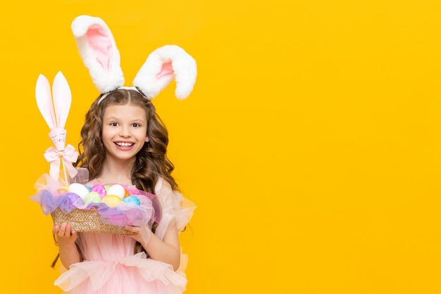 Pascua festiva para niños Una canasta de huevos coloridos para las vacaciones en manos de una adolescente Un niño disfrazado de conejo con orejas largas sobre un fondo amarillo aislado Copiar espacio banner