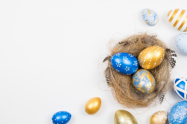 Pascua oro decorado huevos en nido aislado en superficie blanca. Concepto mínimo de pascua.