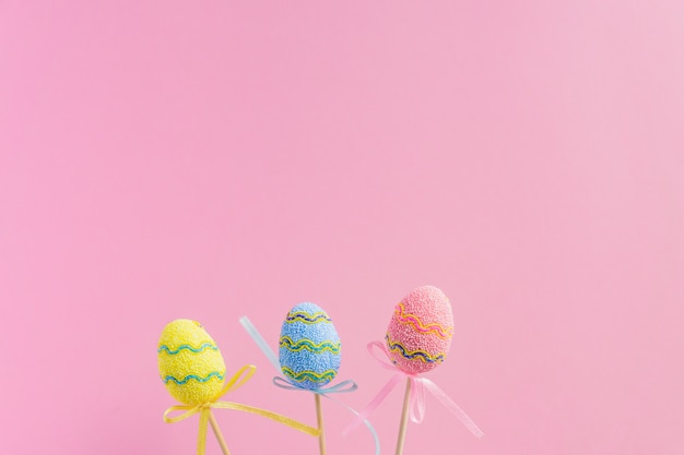 Pascua púrpura, amarillo y azul decorado huevos de pie sobre un palo de madera sobre fondo rosa. Concepto mínimo de pascua. Tarjeta de pascua feliz