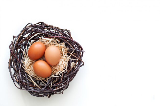 ¡Pascua de Resurrección! Huevos de gallina en un nido con ramas, agricultura. Huevos de Pascua en la mesa en el nido. Beige huevos de Pascua. Huevos sobre un fondo blanco. Granja. Comida de nido de pollo. Alimentación saludable.