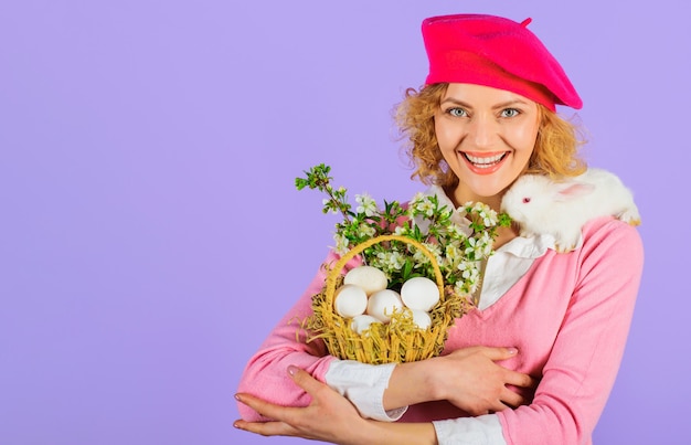 Pascua de Resurrección. Mujer feliz con conejo blanco y huevos de canasta. Niña con conejito.