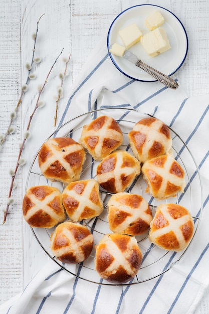 Pascua tradicional hot cross bollos caseros en bandeja de madera con ramas de lino textil y sauce sobre fondo de madera blanca. Enfoque selectivo. Vista superior. Copia espacio