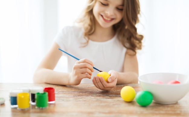 Pascua, vacaciones y concepto de niño - cerca de niña coloreando huevos para Pascua