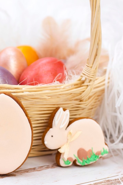 Pascua vacaciones. Huevos de colores en una canasta. Conejo y huevos de pan de jengibre de Pascua. sobre un fondo claro. foto vertical