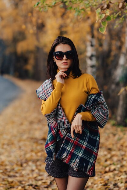 Paseo elegante elegante de la chica joven en el parque colorido del otoño en gafas de sol