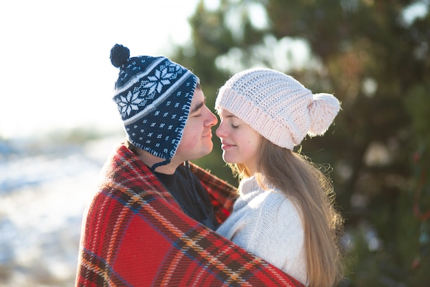 Paseo invernal por el bosque. El chico con la chica besada envuelto en una tela escocesa roja a cuadros