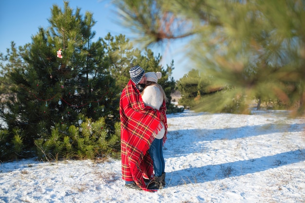 Paseo invernal por el bosque. El chico de la manta roja a cuadros envuelve a la chica para que se caliente