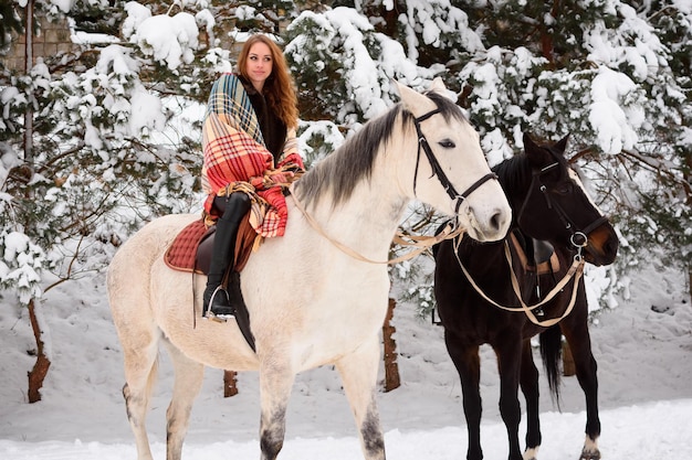 Paseo invernal a caballo por el bosque Una chica con un abrigo de piel y una bufanda brillante en la nieve