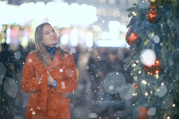 Paseo navideño en la ciudad / niña adulta camina en la ciudad nocturna en una noche festiva, las luces de la ciudad son año nuevo