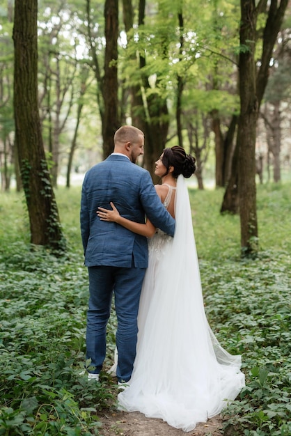 Paseo nupcial de la novia y el novio en el bosque caducifolio en verano