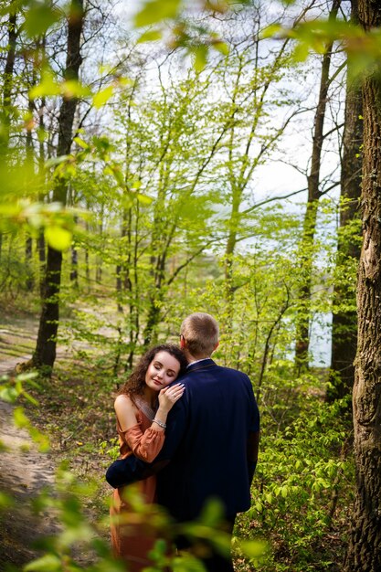 Foto paseo romántico de una pareja joven en un bosque verde, clima cálido de primavera. chico y chica abrazándose en la naturaleza