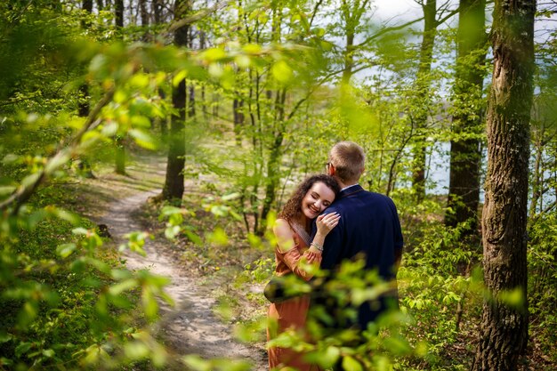 Paseo romántico de una pareja joven en un bosque verde, clima cálido de primavera. Chico y chica abrazándose en la naturaleza
