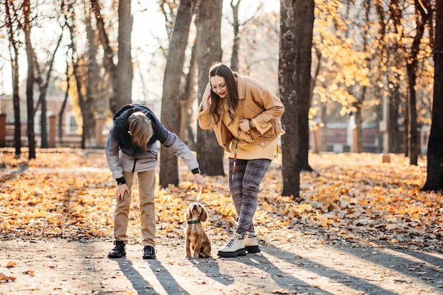 Paseos de otoño con la familia Feliz madre de familia y su hijo adolescente divirtiéndose con un cachorro de cocker spaniel en el parque de otoño