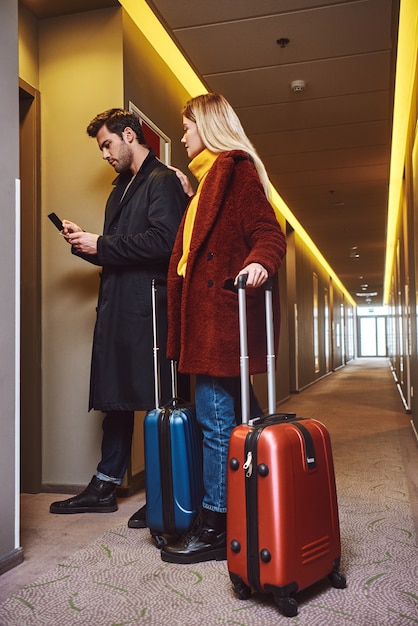 En el pasillo del hotel. Pareja joven entra al piso del hotel con su equipaje y charlando. Longitud total