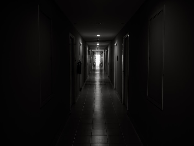 Pasillo oscuro y misterioso en el edificio Perspectiva de la habitación de la puerta en un edificio solitario y tranquilo con pasarela que se dirige a la luz al final del camino estilo blanco y negro esperanza valiente y concepto de miedo