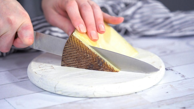 Paso a paso. Cortar un queso gourmet en una tabla de cortar blanca con un cuchillo de cocina.