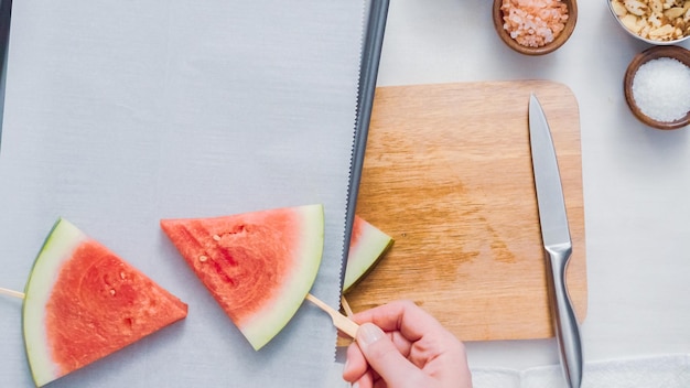 Paso a paso. Deslizar el palito de paleta de madera en la cuña de sandía para hacer paletas heladas de sandía.