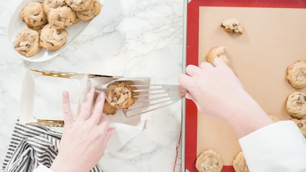 Paso a paso. Endecha plana. Empaquetado de galletas con trocitos de chocolate caseras en una pequeña caja de regalo.