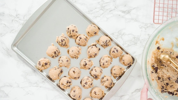 Paso a paso. Endecha plana. Sacar galletas de chispas de chocolate caseras con una cuchara de masa de metal en la bandeja para hornear.