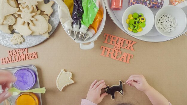 Paso a paso. Madre e hija decorando galletas de azúcar de Halloween con glaseado real de colores.