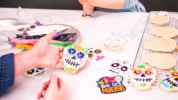 Paso a paso. Madre e hija decorando galletas de calaveras de azúcar con glaseado real para la festividad del Día de los Muertos.