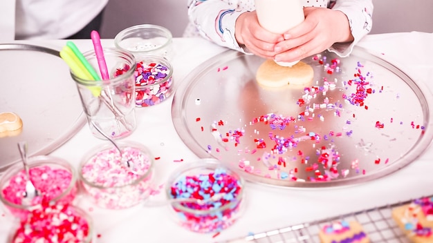 Foto paso a paso. niña regalando galletas de azúcar con glaseado real y chispas para el día de san valentín.