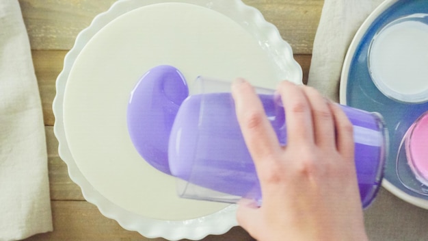 Paso a paso. Pastre shef haciendo tarta de mousse con glaseado de espejo morado y decorada con flores de color rosa chocolate.