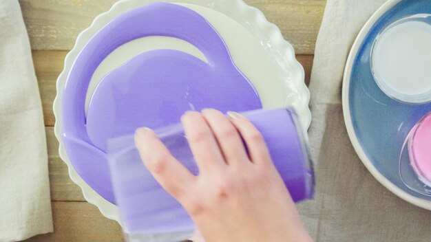 Paso a paso. Pastre shef haciendo tarta de mousse con glaseado de espejo morado y decorada con flores de color rosa chocolate.