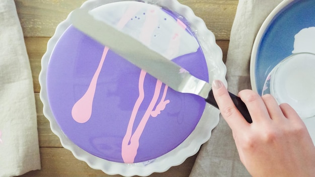 Paso a paso. Pastre shef haciendo tarta de mousse con glaseado de espejo morado y decorada con flores de color rosa chocolate.