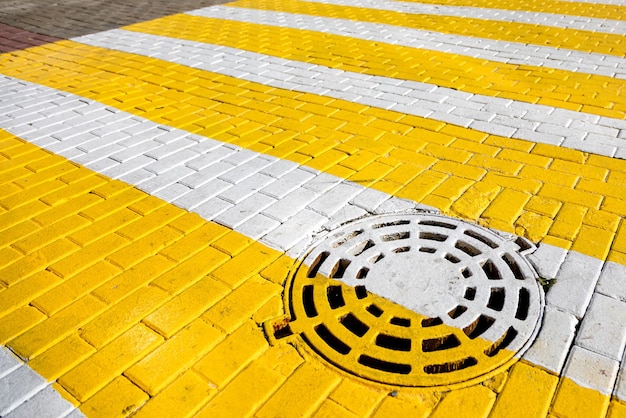 Foto paso de peatones blanco y amarillo con trampilla de alcantarillado pluvial