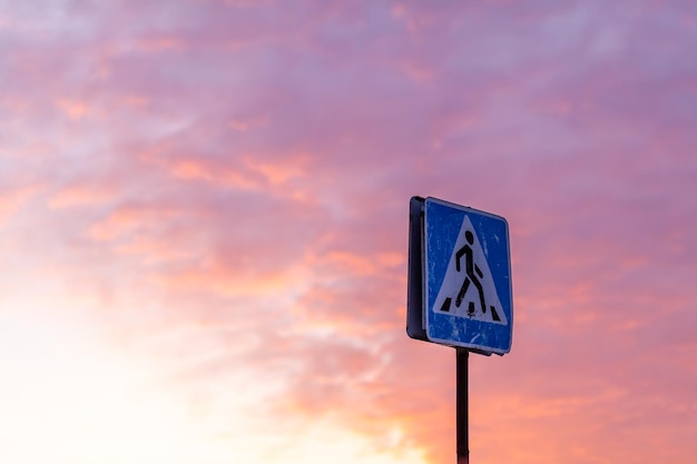 Paso de peatones de señal de tráfico en el fondo del cielo. Un cartel gastado en el fondo de la puesta de sol advierte a los conductores sobre un paso de peatones. Precaución en el camino.