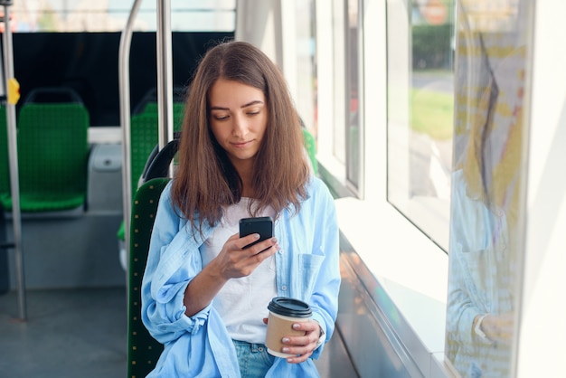 Passageira bonita senta-se com smartp aprimorar enquanto se move no moderno bonde ou metrô. Viagem no transporte público.