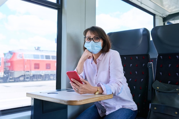 Passageira com máscara facial médica dentro do trem local Mulher de meia-idade com mochila de smartphone sentada no trem perto da janela Transporte ferroviário viagem viagem conceito de pessoas