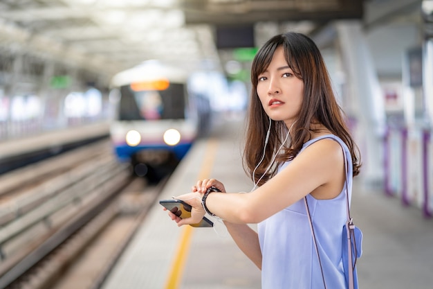 Passageira jovem asiática checando as horas e esperando a amiga no trem do metrô