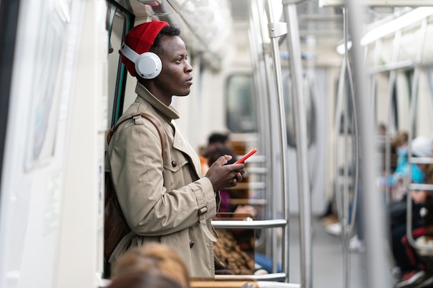 Passageiro afro-americano no metrô, usando um smartphone móvel, ouve música com fones de ouvido