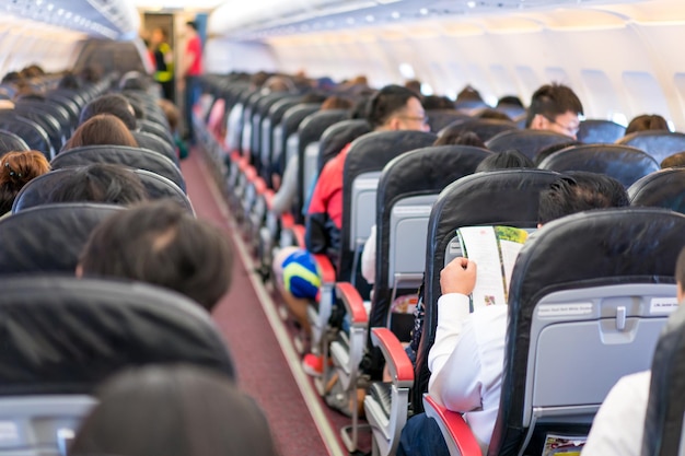 Passageiro asiático lendo a revista / menue / catálogo enquanto aguarda a decolagem do avião em voo.