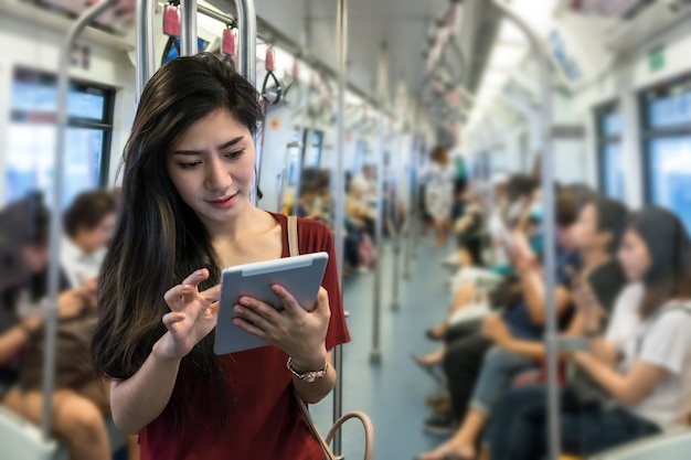 Passageiro da mulher asiática com roupa casual usando o tablet de tecnologia