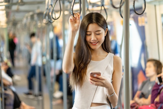 Passageiro de jovem mulher asiática usando rede social via celular inteligente no metrô