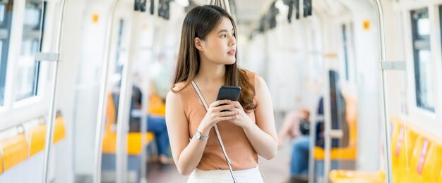Passageiro de jovem mulher asiática usando um telefone celular inteligente e olhando para fora do metrô