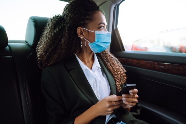 Passageiro de mulher relaxada na máscara médica protetora no carro táxi.