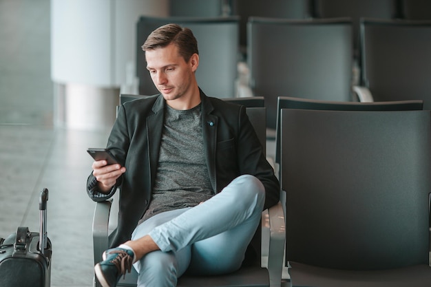 Passageiro em um saguão de aeroporto esperando por avião de voo jovem com smartphone em espera de aeroporto