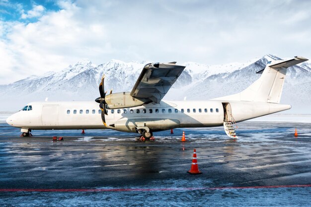 Passagier-Turboprop-Flugzeug auf dem Vorfeld des Winterflughafens vor dem Hintergrund hoher malerischer Berge