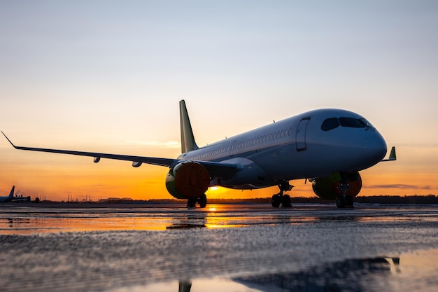 Passagierflugzeug auf dem Vorfeld des Flughafens vor dem Hintergrund des Sonnenuntergangs mit Reflexion in einer Pfütze