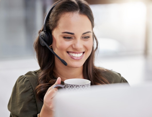 Foto passando por mais um dia de sucesso foto de um jovem agente de call center tomando café enquanto trabalhava em um computador em um escritório