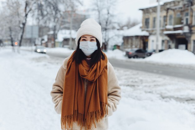 Passant asiatische Frau in einer medizinischen Schutzmaske im Freien. Eine Frau auf der Straße im Winter schützt die Atemwege vor der Coronavirus-Epidemie.