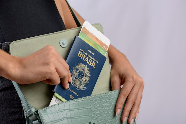 Passaporte brasileiro Mãos colocando passaporte brasileiro na bolsa feminina verde